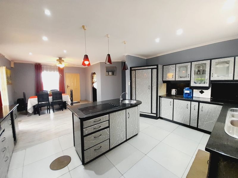 Open-plan kitchen and dining area featuring a central island with integrated hob, modern cabinetry, and tiled flooring throughout.