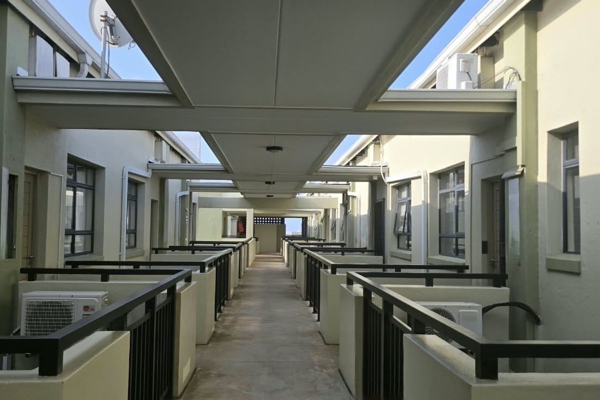 A well-maintained outdoor apartment complex walkway featuring covered roofing, metal safety railings, and external air conditioning units.