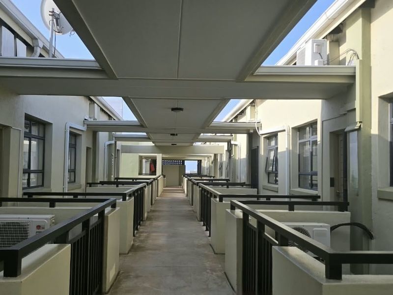 A well-maintained outdoor apartment complex walkway featuring covered roofing, metal safety railings, and external air conditioning units.