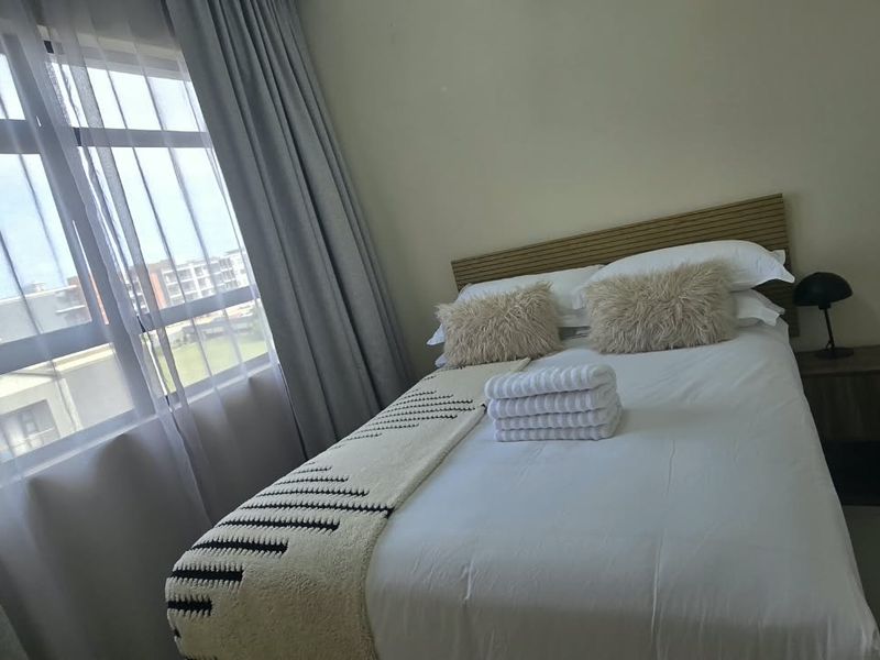 A well-lit bedroom featuring tiled flooring, a large window with curtains, and a built-in wardrobe.