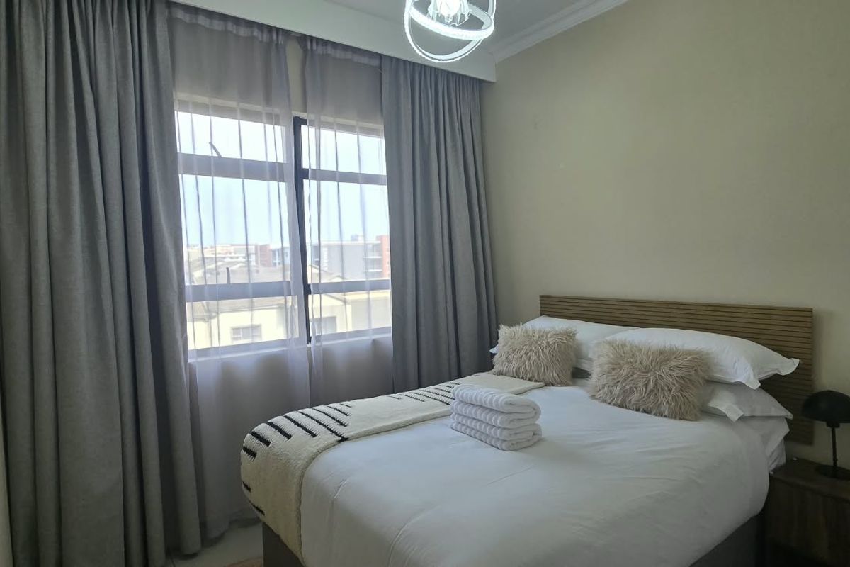 A well-lit bedroom featuring a large window with floor-to-ceiling curtains and a central ceiling light fixture.