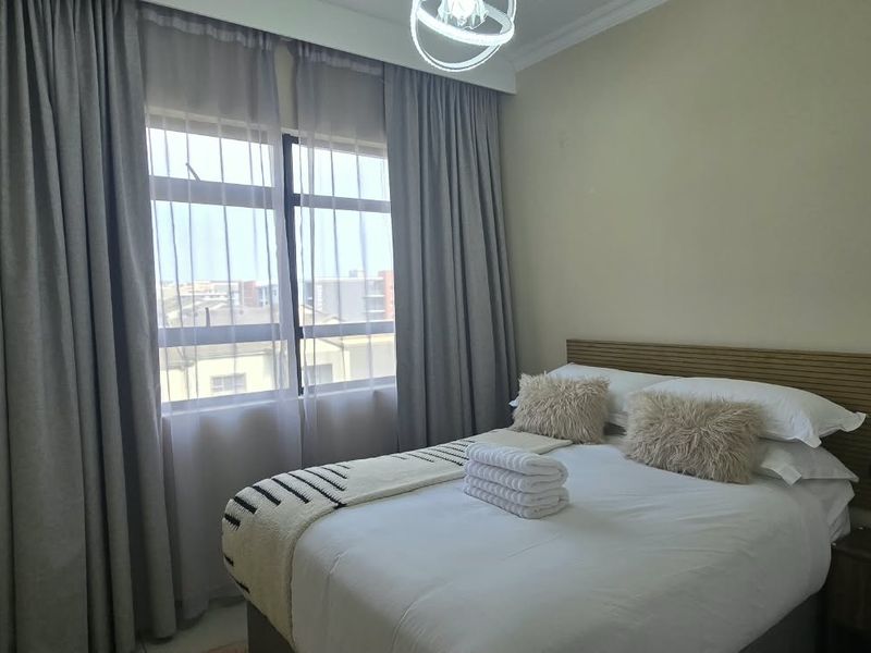 A well-lit bedroom featuring a large window with floor-to-ceiling curtains and a central ceiling light fixture.