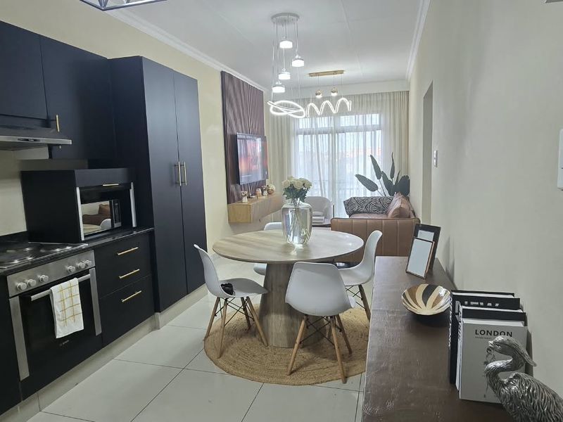 Modern open-plan apartment featuring a sleek kitchen with dark cabinetry, integrated appliances, and a seamless flow into the dining and living area.