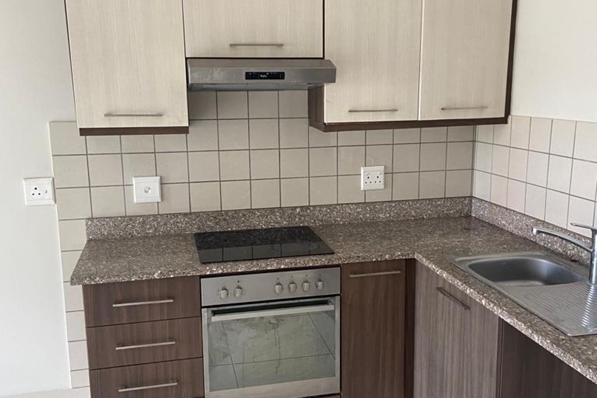 A clean, functional kitchen featuring two-tone cabinetry, stone countertops, integrated oven and hob, and a tiled backsplash.