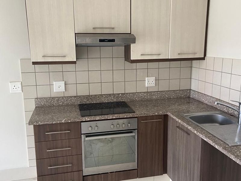 A clean, functional kitchen featuring two-tone cabinetry, stone countertops, integrated oven and hob, and a tiled backsplash.