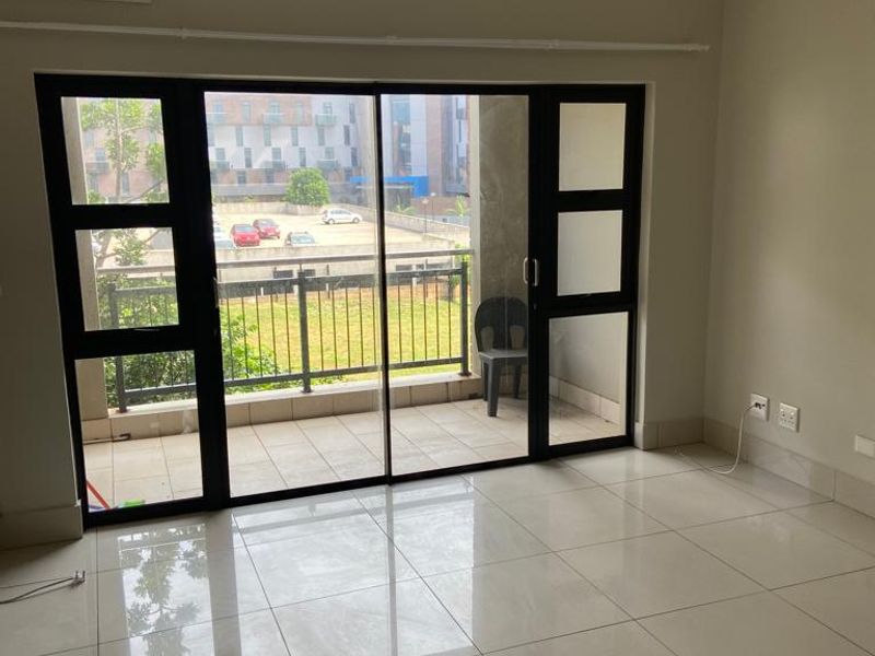 An empty living room featuring large sliding glass doors leading to a balcony, tiled flooring, and a wall-mounted air conditioning unit.