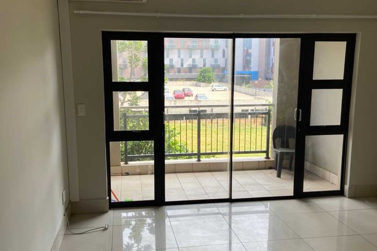 Bright living area featuring large sliding glass doors leading to a private balcony, tiled floors, and a wall-mounted air conditioning unit.