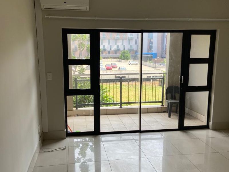 Bright living area featuring large sliding glass doors leading to a private balcony, tiled floors, and a wall-mounted air conditioning unit.