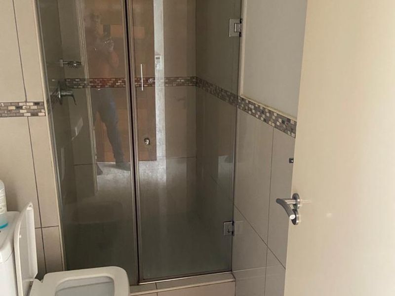 A functional bathroom featuring a glass-enclosed shower, tiled walls with a decorative mosaic border, and a standard toilet.