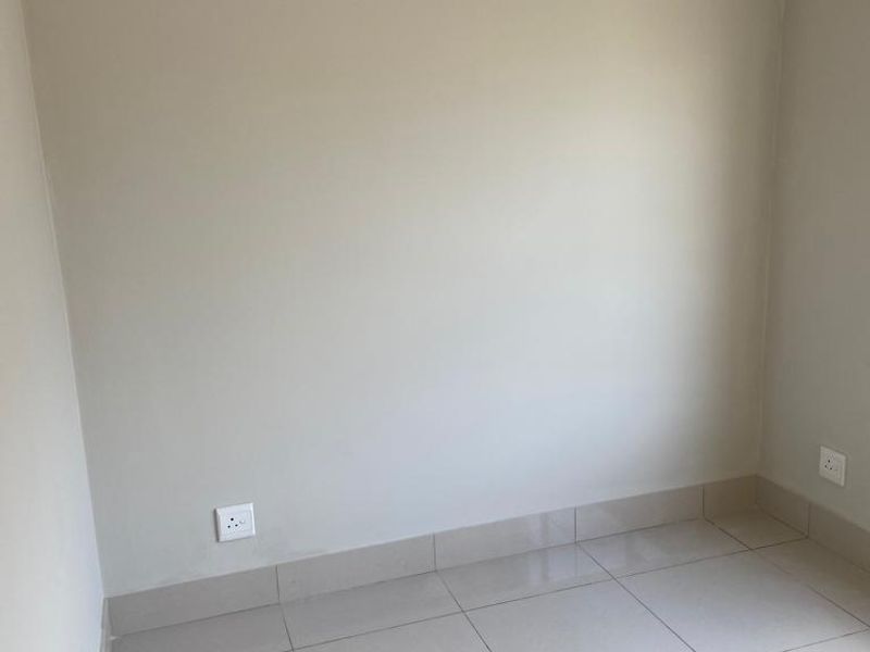 A clean, empty bedroom featuring neutral tiled flooring, matching skirting boards, and installed electrical power outlets.
