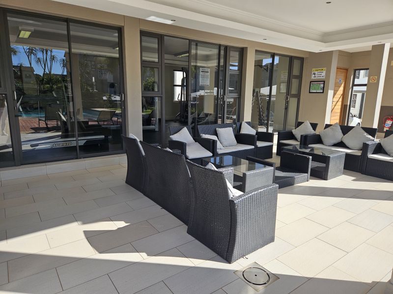 A spacious covered patio area featuring tiled flooring and large sliding glass doors providing access to the interior gym facility.