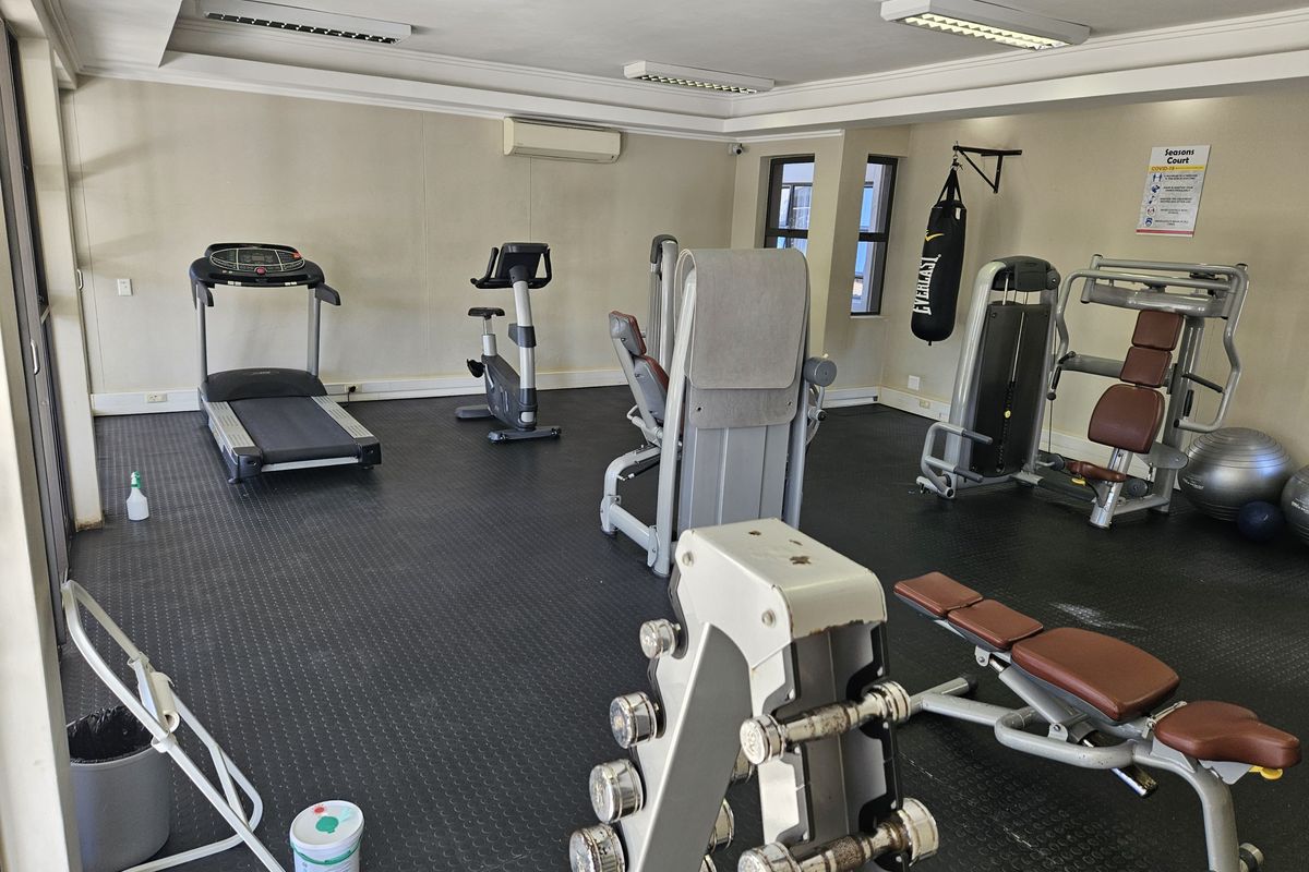 A functional apartment complex gym featuring rubber flooring, split-system air conditioning, and various fixed exercise equipment.
