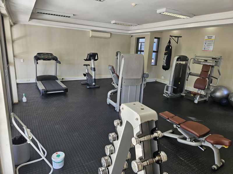 A functional apartment complex gym featuring rubber flooring, split-system air conditioning, and various fixed exercise equipment.