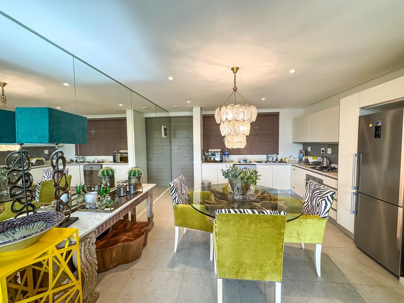 Modern open-plan kitchen and dining area featuring sleek built-in cabinetry, integrated appliances, tiled flooring, and a large feature mirror wall.
