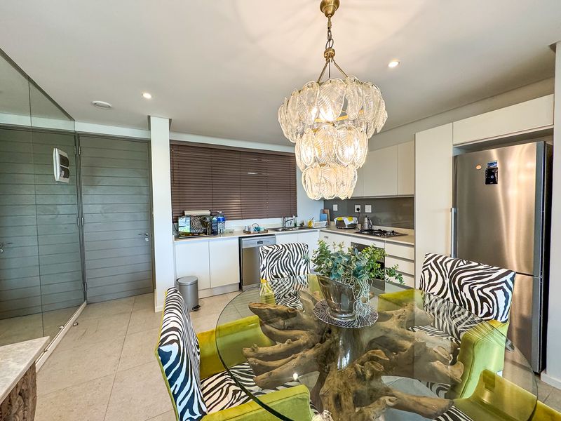 Modern open-plan kitchen and dining area featuring sleek cabinetry, integrated appliances, tiled flooring, and a statement chandelier.