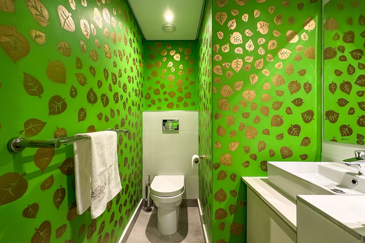 A compact bathroom featuring a wall-mounted toilet with a concealed cistern, a modern vanity basin, and distinctive leaf-patterned wallpaper.