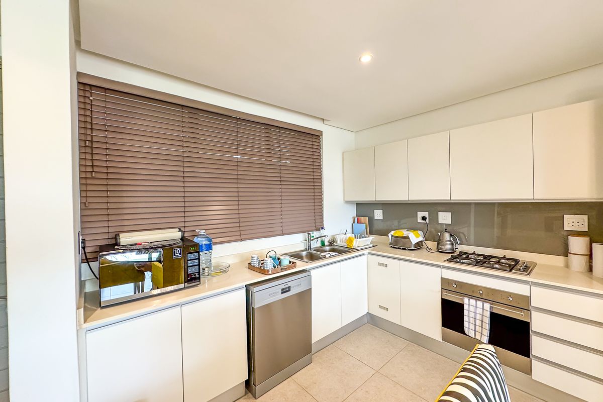 Modern kitchen featuring sleek white cabinetry, integrated dishwasher, gas hob, built-in oven, and a glass splashback with neutral tiled flooring.