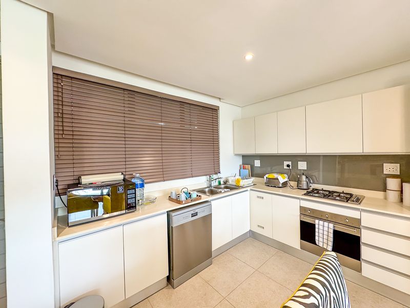 Modern kitchen featuring sleek white cabinetry, integrated dishwasher, gas hob, built-in oven, and a glass splashback with neutral tiled flooring.