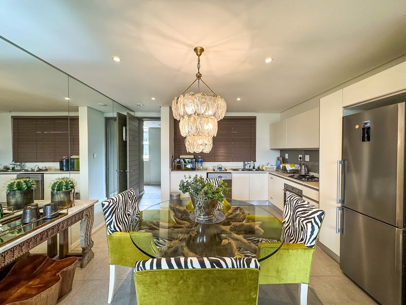 Modern open-plan kitchen and dining area featuring sleek cabinetry, integrated appliances, tiled flooring, and a large mirrored wall enhancing the sense of space.