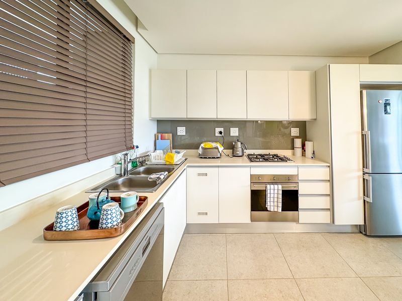 Modern kitchen featuring white cabinetry, stainless steel appliances, gas hob, built-in oven, and tiled flooring with a neutral glass splashback.