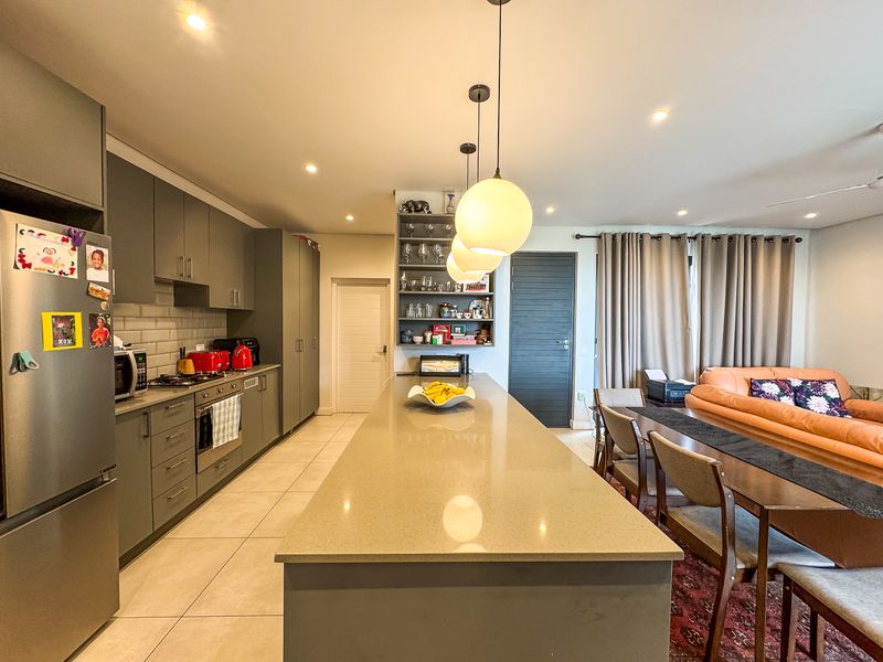 Modern open-plan living area featuring a sleek kitchen with a large island, quartz countertops, grey cabinetry, and integrated appliances, flowing into the dining space.