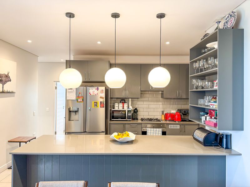 Modern kitchen featuring a central island with quartz countertops, grey cabinetry, subway tile backsplash, and integrated gas cooktop with oven.