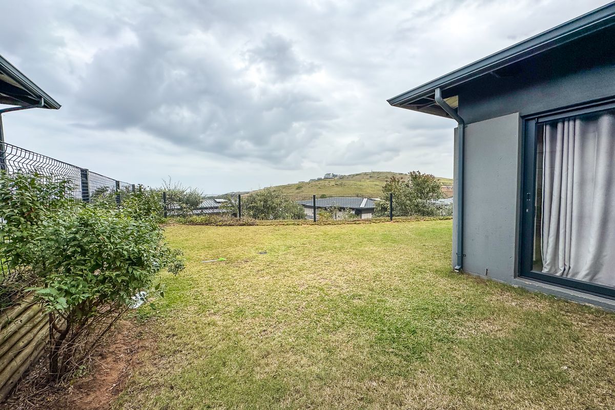 A private rear garden area featuring a well-maintained lawn, metal perimeter fencing, and direct access to the home via a sliding glass door.