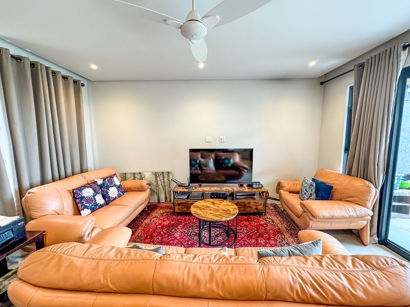 A comfortable living room featuring a ceiling fan, recessed lighting, and large sliding glass doors providing access to the outdoor area.