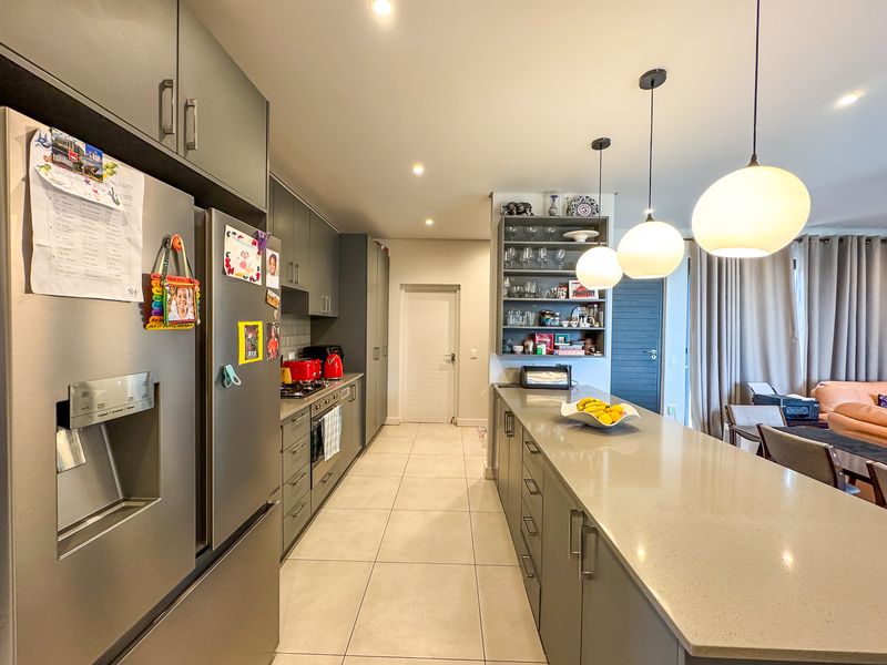 Modern kitchen featuring a large stone island, sleek grey cabinetry, integrated appliances, and stylish pendant lighting, flowing into an open-plan living area.