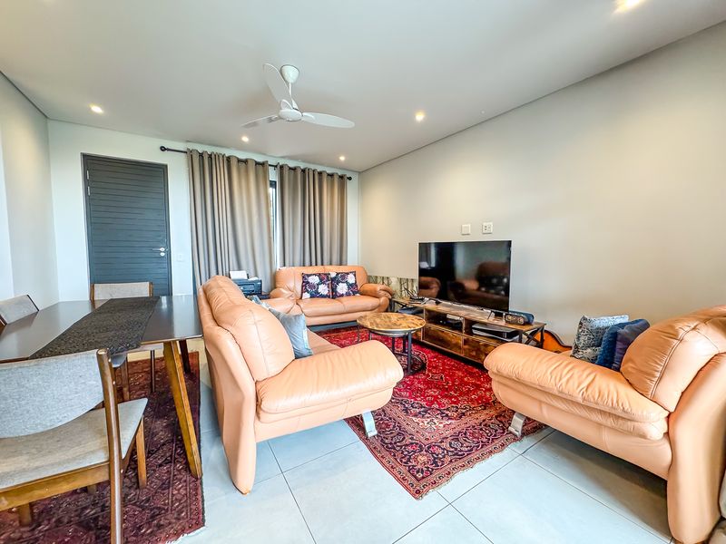 An open-plan living and dining area featuring neutral tiled flooring, recessed ceiling lighting, and a ceiling fan.