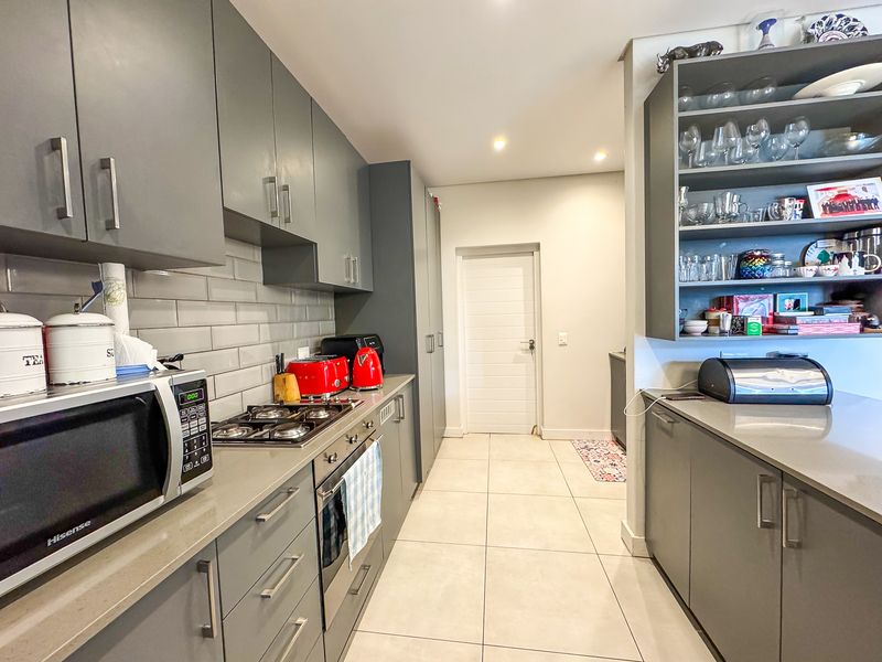 Modern kitchen featuring sleek grey cabinetry, stone countertops, gas hob, built-in oven, and stylish subway tile backsplash with ample open shelving.