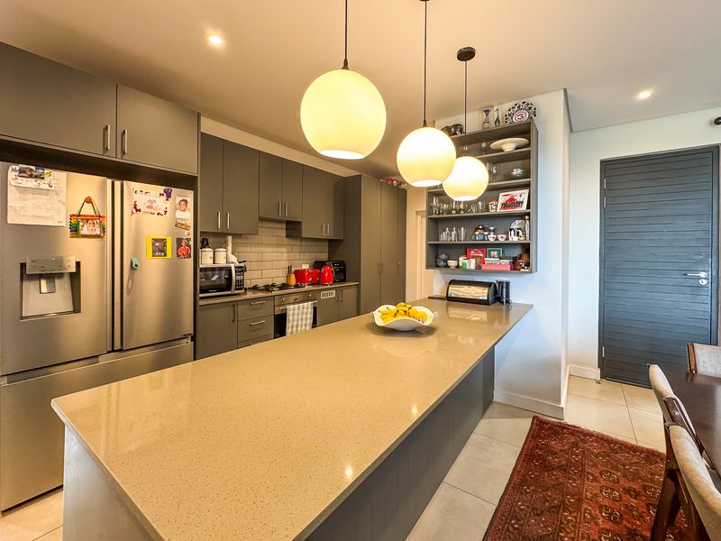 Modern kitchen featuring a large quartz island, dark grey cabinetry, subway tile backsplash, and integrated appliances with stylish pendant lighting.
