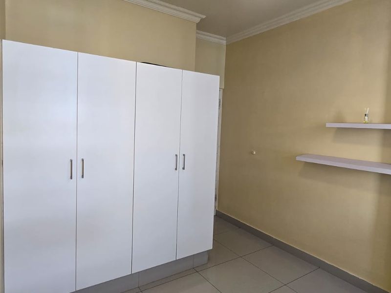 A clean, empty bedroom featuring a large white built-in wardrobe, modern floating shelves, neutral wall paint, and tiled flooring.