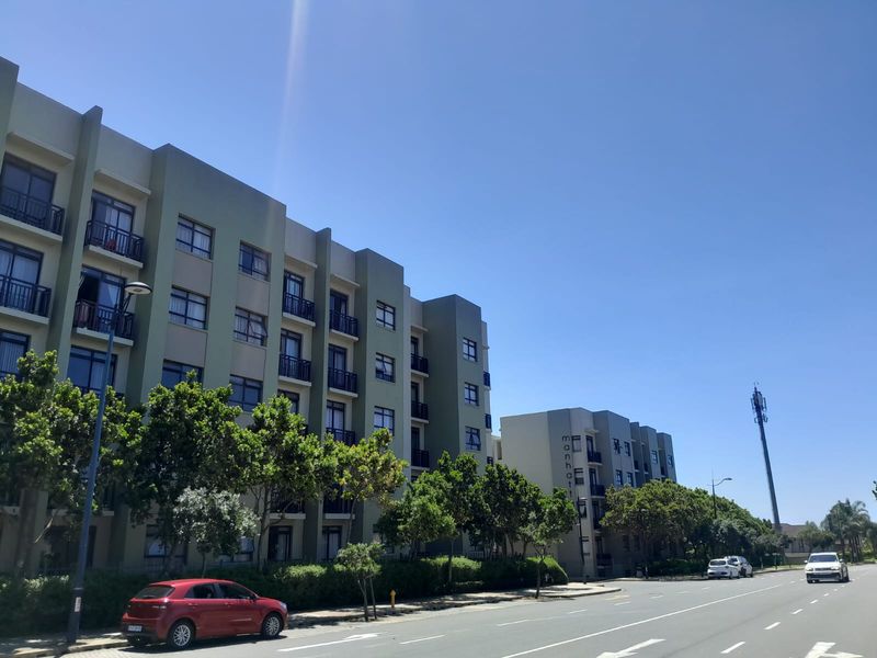 A street-level view of a modern multi-story apartment complex featuring balconies and well-maintained exterior facades.