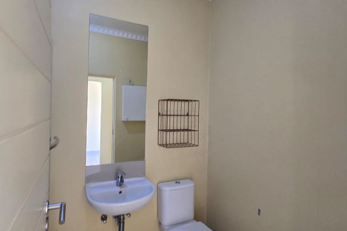 A compact, functional bathroom featuring a wall-mounted basin, toilet, and mirror, presenting a clean and neutral space ready for updates.