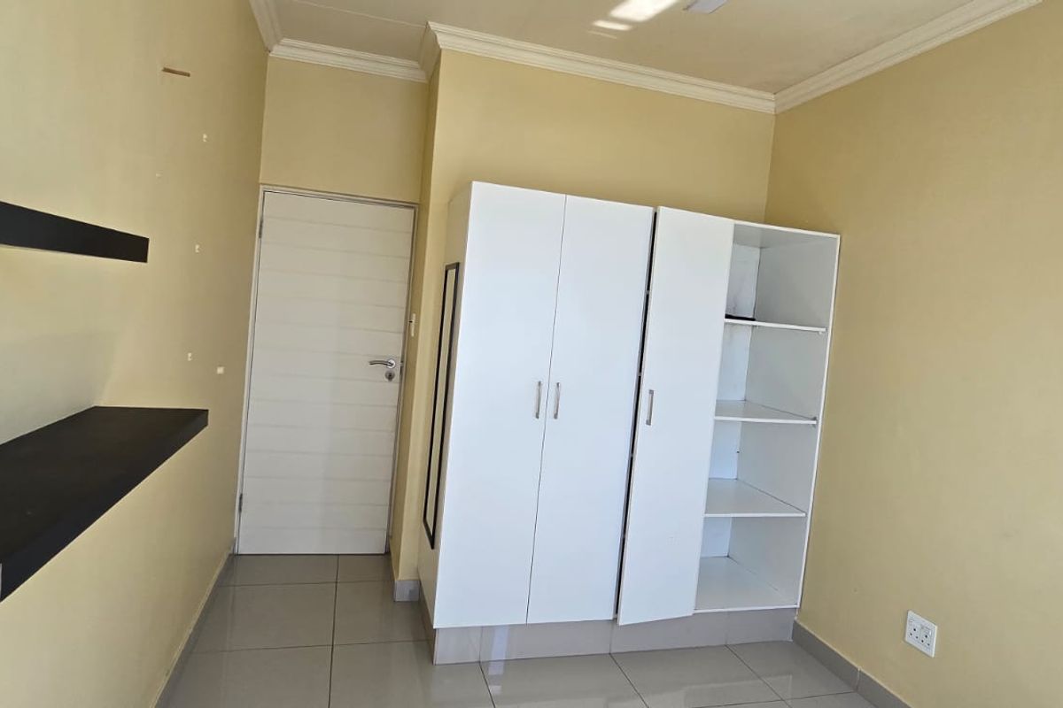 A bedroom featuring tiled flooring, a built-in wardrobe, and wall-mounted floating shelves, with some minor wall surface imperfections visible.
