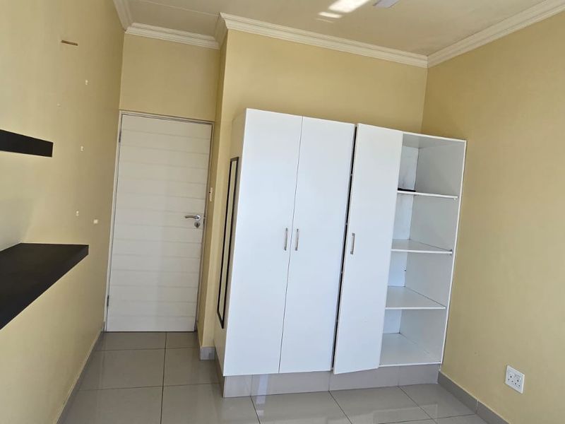 A bedroom featuring tiled flooring, a built-in wardrobe, and wall-mounted floating shelves, with some minor wall surface imperfections visible.
