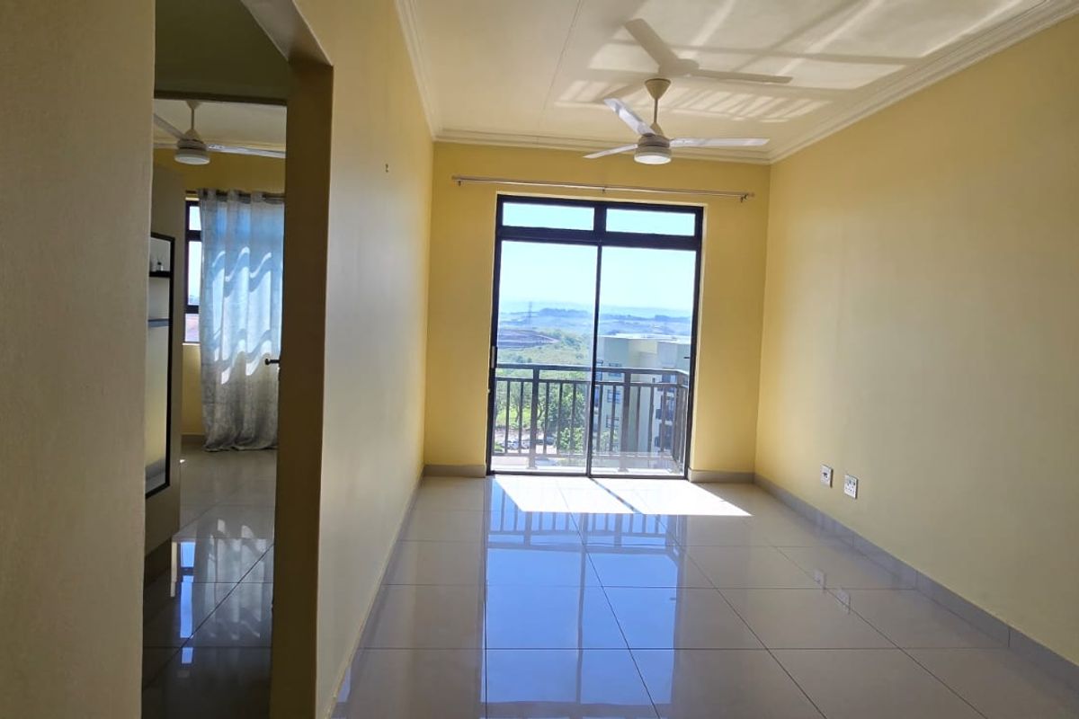 An empty, well-lit living room featuring tiled floors, a ceiling fan, and a sliding glass door leading to a balcony with scenic views.