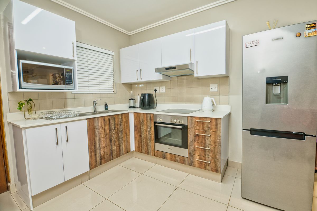 Modern kitchen featuring white and wood-grain cabinetry, integrated appliances, tiled backsplash, and neutral floor tiles in a clean, well-maintained layout.
