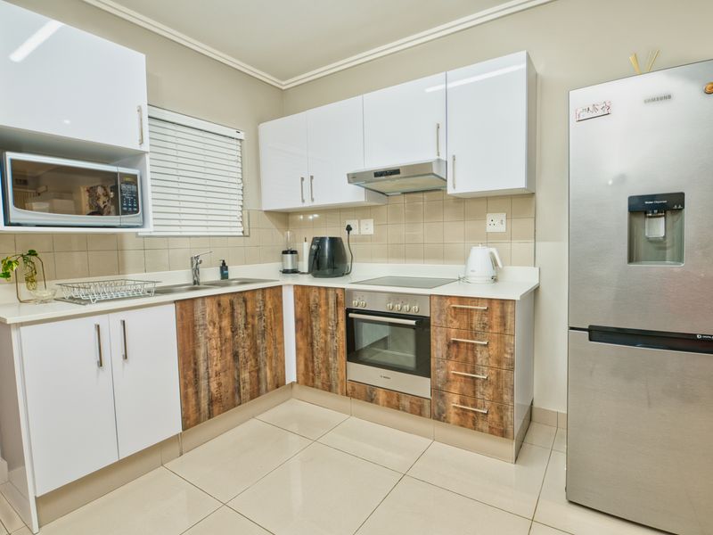 Modern kitchen featuring white and wood-grain cabinetry, integrated appliances, tiled backsplash, and neutral floor tiles in a clean, well-maintained layout.