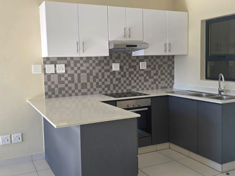 Modern kitchen featuring two-tone cabinetry, stone countertops, mosaic tile backsplash, and integrated appliances including an electric hob and oven.