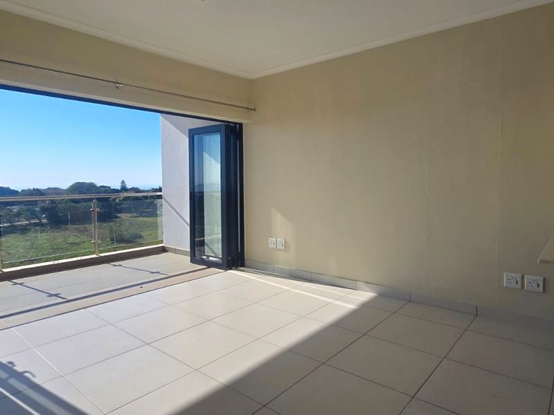 Open plan living area featuring tiled floors, modern kitchen cabinetry with mosaic backsplash, and bi-fold doors opening onto a balcony with scenic views.