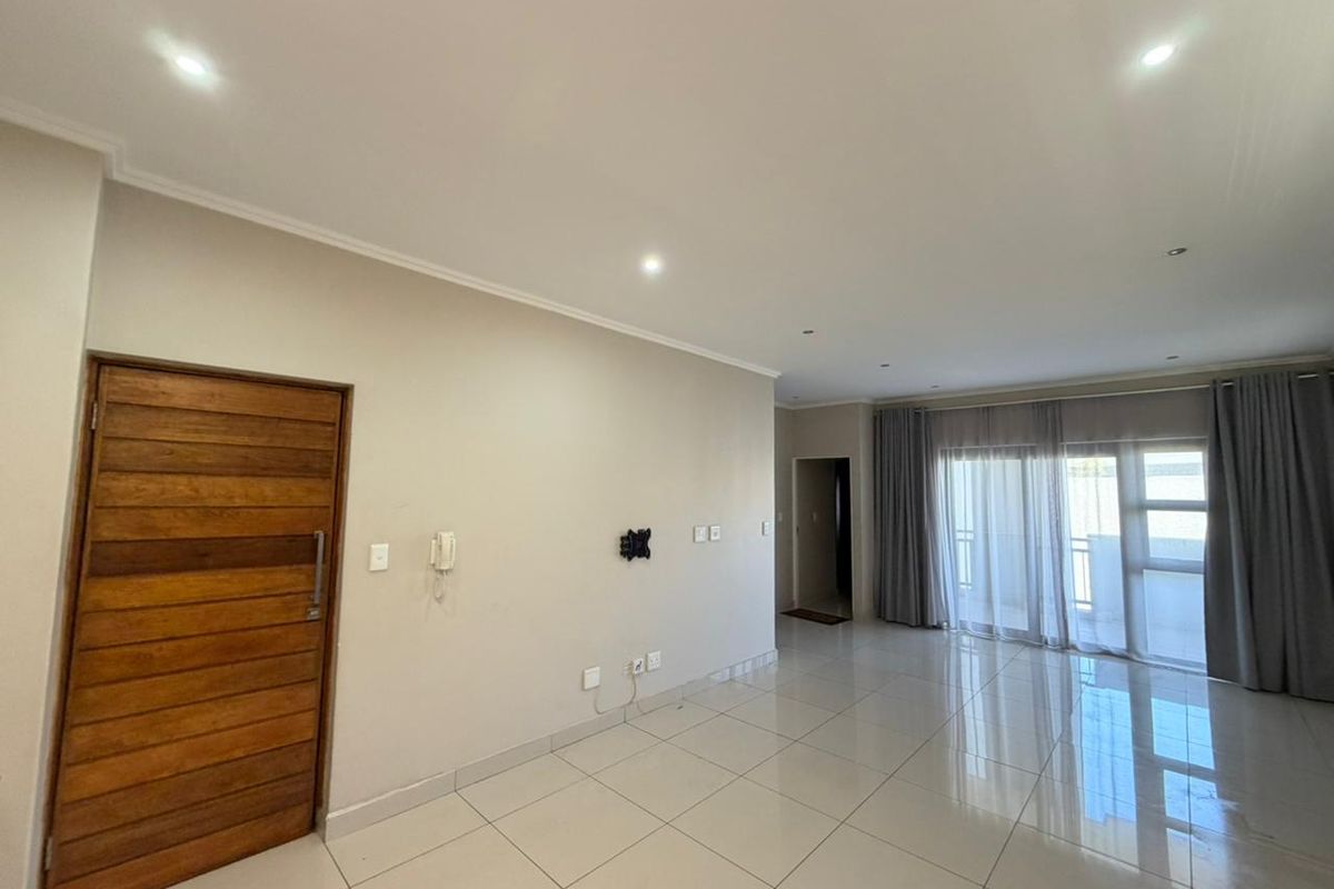 Spacious, open-plan living area featuring neutral tiled flooring, recessed downlighting, and large sliding glass doors leading to an outdoor space.
