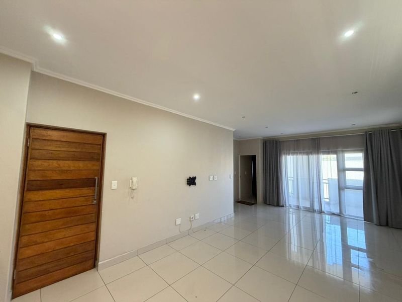 Spacious, open-plan living area featuring neutral tiled flooring, recessed downlighting, and large sliding glass doors leading to an outdoor space.