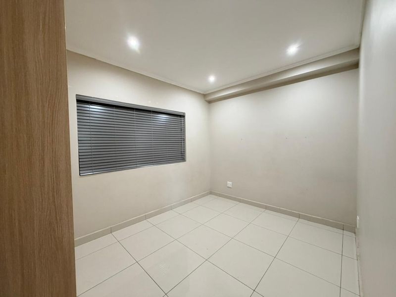A clean, empty bedroom featuring neutral tiled flooring, recessed downlighting, and fitted venetian blinds, offering a blank canvas for personalization.