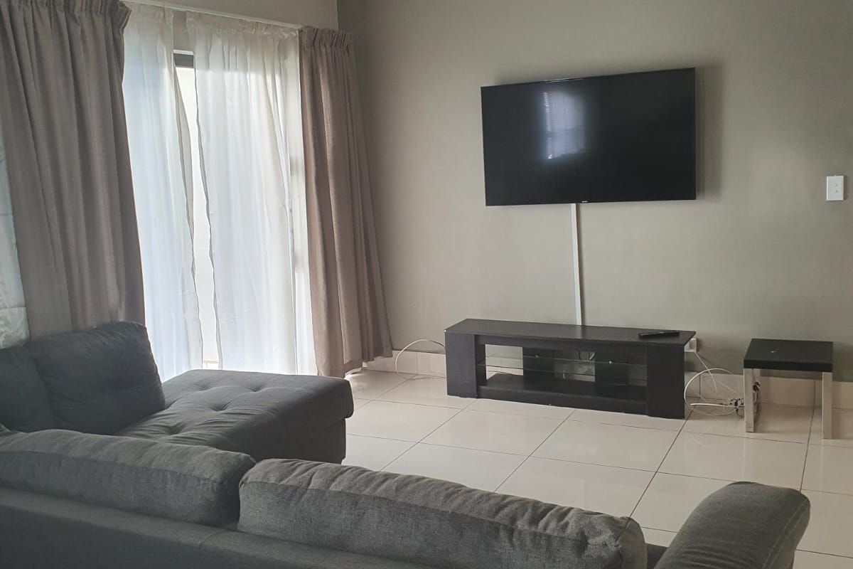 A living room featuring neutral tiled flooring, recessed downlights, and a sliding glass door providing access to the exterior.