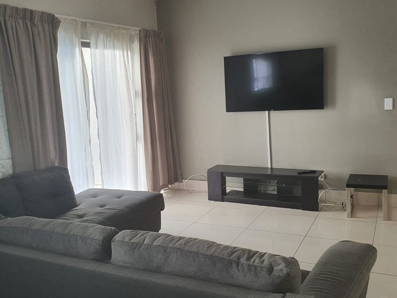 A living room featuring neutral tiled flooring, recessed downlights, and a sliding glass door providing access to the exterior.