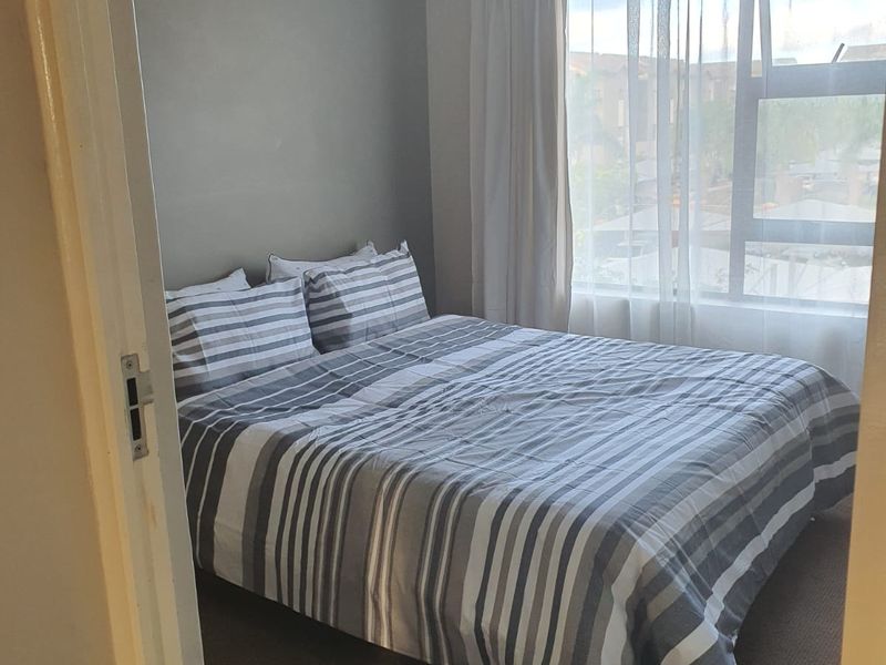 A cozy bedroom featuring neutral wall tones, carpeted flooring, and a large window allowing for natural light.