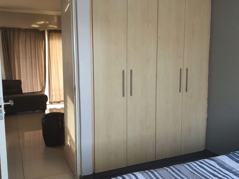 A bedroom featuring built-in wooden wardrobes and carpeted flooring, with a doorway leading to an adjacent living area.
