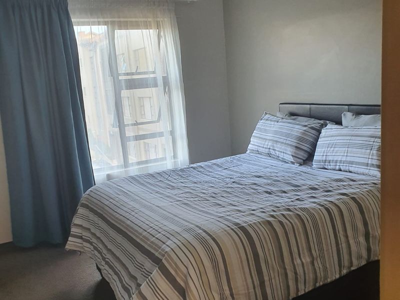 A standard bedroom featuring neutral wall tones, carpeted flooring, and a window with a curtain rail.